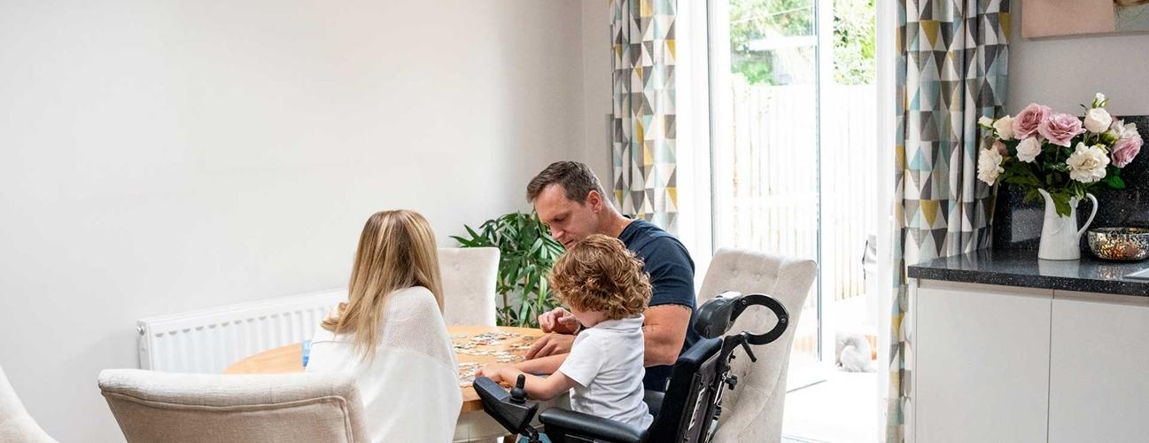 Child with muscular dystrophy with parent's doing a puzzle at table